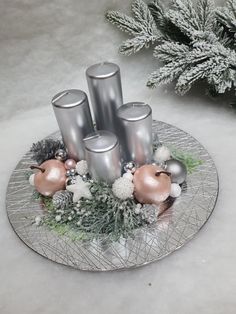 some silver candles are sitting on a glass plate with snow and pine branches in the background