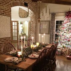 the table is set for christmas dinner with candles on it, and an image of a tree in the background