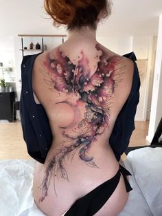 the back of a woman's body with flowers and feathers tattooed on her stomach