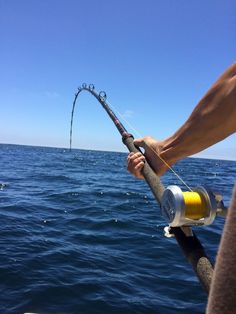 a man holding a fishing rod while standing on the side of a boat in the ocean