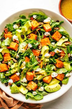 a salad with lettuce, carrots and feta cheese in a white bowl