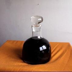 a black bottle sitting on top of a yellow table cloth next to a white wall