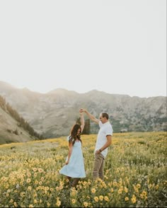 a man and woman dancing in a field with mountains in the background