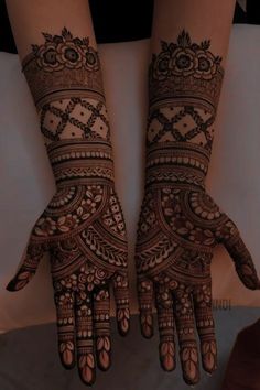 two hands with henna tattoos on them, one is showing the intricate design and the other has flowers