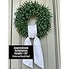 a wreath on the side of a door with a white bow hanging from it's side