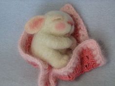 a small stuffed animal with a pink blanket on it's back, sitting in the middle of a gray background