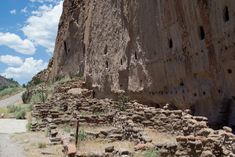 an old stone wall with holes in it near a dirt road and mountain side under a partly cloudy blue sky