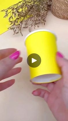 a person holding a yellow cup with pink nail polish on it and another hand reaching for the cup