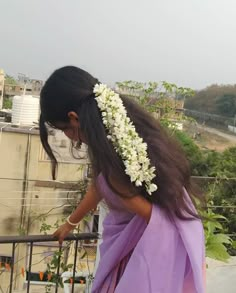 a woman with flowers in her hair on top of a balcony looking down at the ground