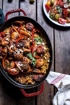 a skillet filled with pasta and meat on top of a wooden table next to olives