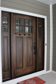 a brown front door with two sidelights and a red rug on the floor next to it