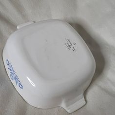 a white porcelain dish with blue flowers on the side and words written on it, sitting on a bed sheet