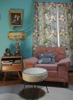 a living room filled with furniture and a window covered in floral drapes next to a lamp