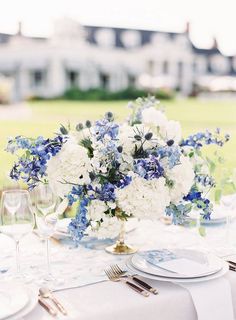 the table is set with blue and white flowers, silverware, and wine glasses