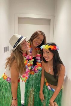 three women in grass skirts and flower leis posing for the camera with their arms around each other