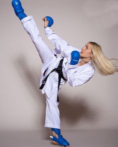 the woman is practicing karate moves with blue gloves on her head and legs, while holding one leg up in the air