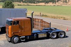 an orange semi truck is parked on the side of the road next to a trailer