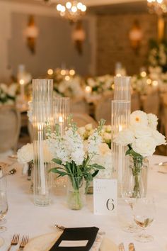 the table is set with white flowers and candles in tall vases on each side