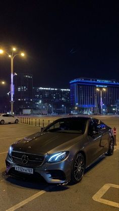 a silver car parked in a parking lot next to tall buildings and street lights at night