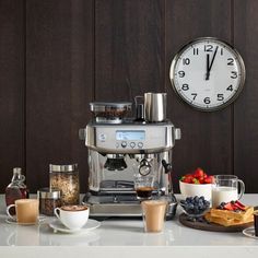 a coffee maker sitting on top of a counter next to cups and plates filled with food