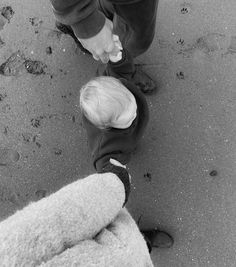 two people standing next to each other on top of a sandy beach with footprints in the sand