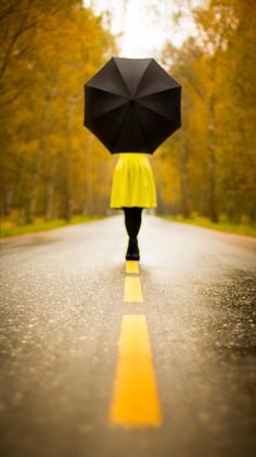 a person walking down the road with an umbrella over their head and yellow raincoat on