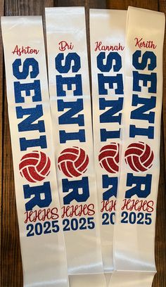 three white banners with red, blue and white volleyball logos are on a wooden table