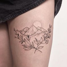 a woman's thigh with a tattoo on her leg and mountains in the background