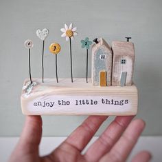 a hand is holding a small book with tiny houses and flowers on it that says, enjoy the little things