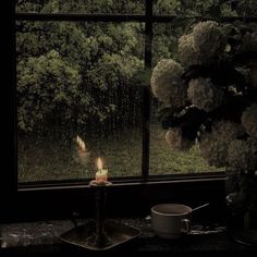 a candle is lit in front of a window with rain coming down on the trees