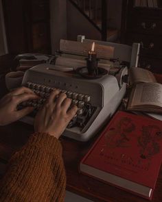 a person typing on an old fashioned typewriter with a book and candle next to it