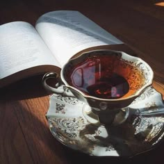 an open book on a wooden table next to a cup of tea and saucer