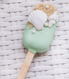 an ice cream on a wooden stick with sea foam and shells in it sitting on a wicker surface