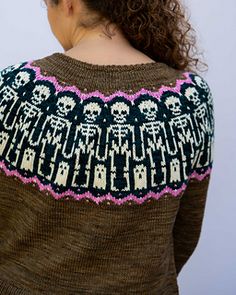 a woman with curly hair wearing a sweater with skulls and bones on the side, back view