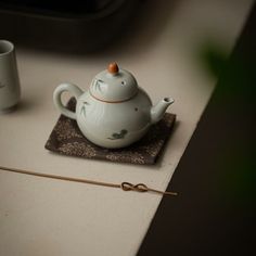 a tea pot sitting on top of a table next to two cups and a stick