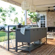 an outdoor kitchen on a deck with potted plants in the center and two hanging lights above it