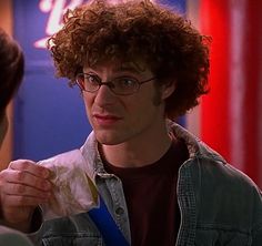 a man with curly hair and glasses is holding something in his hand while looking at another person