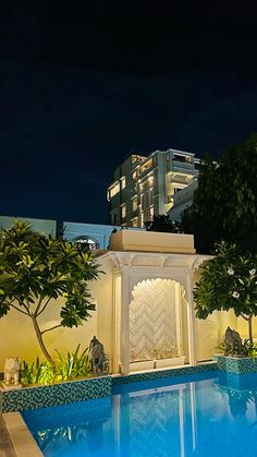 an outdoor swimming pool at night with lights on the building in the backround