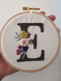 a hand embroidered letter e with flowers and leaves on the front is held up by a person's hand