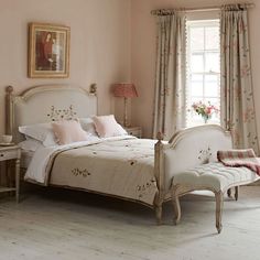 a white bed sitting next to a window in a room with pink walls and curtains