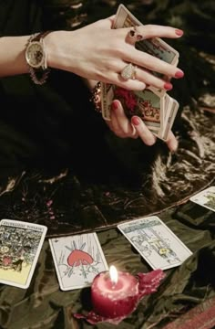 a woman is holding tarot cards in her hand with a candle on the ground