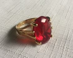 Elegant solitaire red ring set in a gold setting. The gemstone measures .75" by .5"  and it's set in a 18 Kt Electroplated Gold setting. (It says 18 Kt GE inside.) Size 5.75 or maybe 6. Please know that if you don't like the way the ring fits, you can return it; you pay for the shipping, but there's no restocking fee or questions asked, I just refund the ring's cost to you. Please take a look at my storefront at: https://www.etsy.com/shop/FabFinds42?ref=seller-platform-mcnav I have a wide select Red Gem Ring, Gold Ring Big, Red Ring, Red Rings, Red Jewel, Costume Rings, Chunky Ring, Jewels Rings, Chunky Jewelry