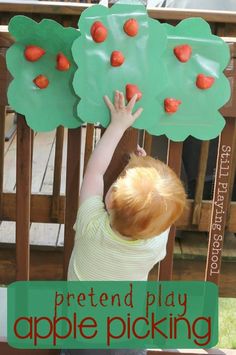 a young child reaching up to pick apples from a tree