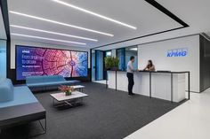 a woman standing at the front desk of a kpmg office with people in it