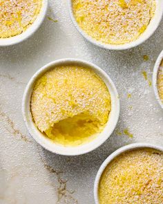 several small white bowls filled with food on top of a marble countertop and covered in powdered sugar