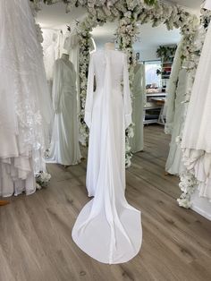 wedding gowns and dresses on display in a bridal room with white flowers hanging from the ceiling