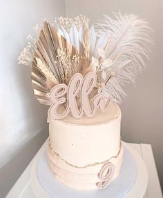 a white cake with feathers on top and the word ella spelled in cursive letters