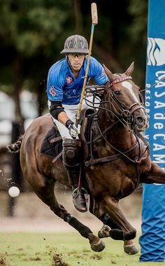 a man riding on the back of a brown horse next to a blue sign and flag