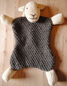 a knitted sheep toy laying on top of a wooden floor with it's eyes closed