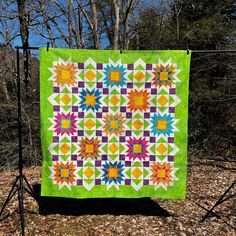 a quilt hanging from a clothes line in the woods with leaves on the ground around it